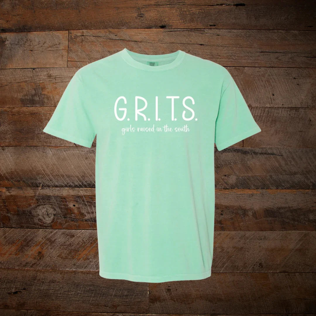 Mint green t-shirt with white text G.R.I.T.S. girls raised in the south, rustic wood background