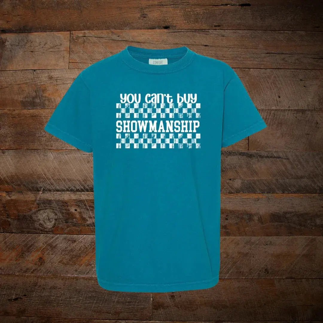 Teal t-shirt with white text 'you can't buy SHOWMANSHIP' and checkerboard pattern, wooden background