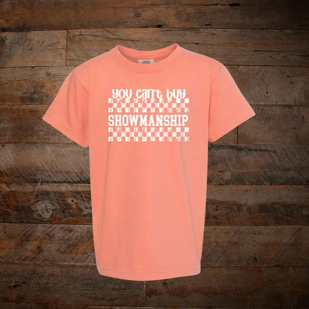 Peach graphic t-shirt with 'You can't buy showmanship' text on wooden background