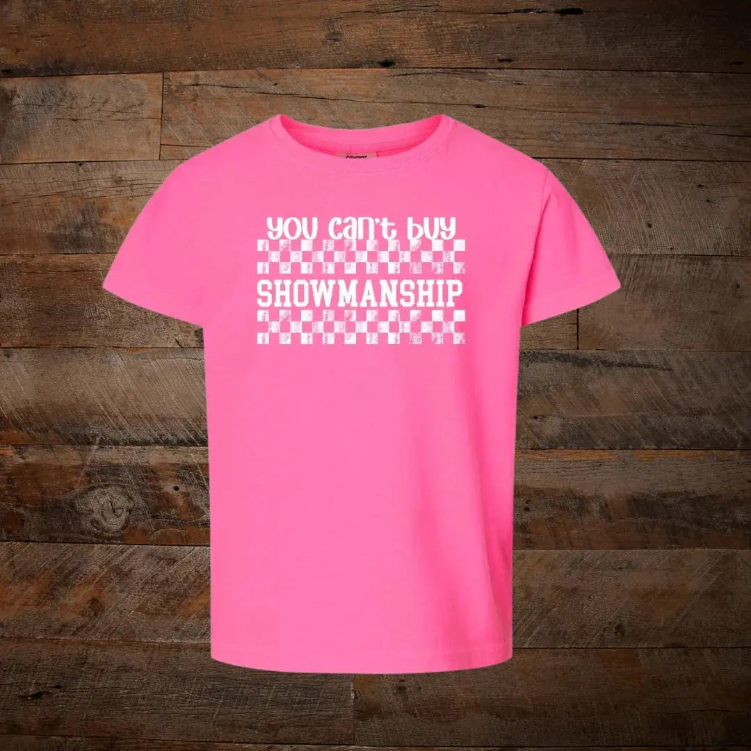 Pink t-shirt with white checkered graphic and 'You can't buy showmanship' text, rustic wood background