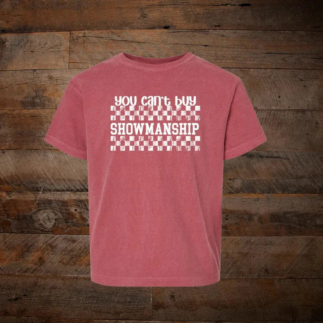 Red graphic t-shirt with 'you can't buy SHOWMANSHIP' text and checkered design on wood background.