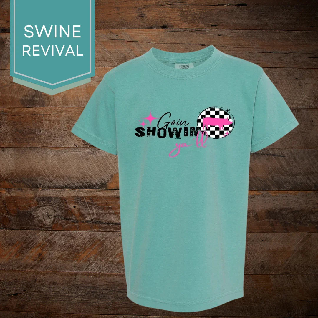 Aqua t-shirt with 'Goin Showin y'all' text and pink pig on a checkerboard graphic, wooden background.